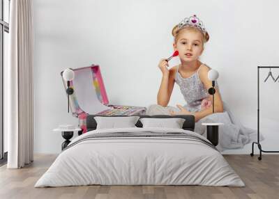 A little girl in a shiny Princess costume is sitting next to a large makeup bag. Wall mural