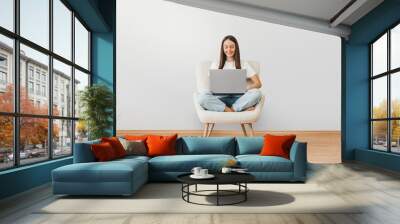 Full length portrait of a happy woman holding laptop computer while sitting on a chair Wall mural