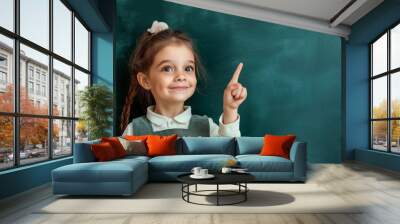 Little girl pointing her finger up on a green chalkboard background, a school concept
 Wall mural