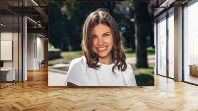 Portrait of a young cute girl in a white T-shirt with a smile in the park. Attractive girl smiling in the park and looking at the camera Wall mural