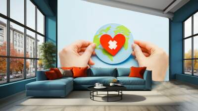 World health day concept. Female hands hold a paper model of the globe with a heart Wall mural