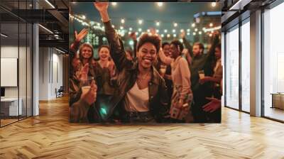 A joyous African American woman raises her hand high, celebrating with a diverse crowd at a festive outdoor event. Wall mural