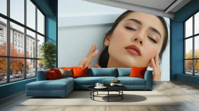 Beauty portrait of a young woman: a woman touches the skin of her face with her fingertips, her eyes closed in pleasure. Wall mural