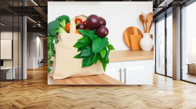 Fabric bag, shopper with fresh vegetables and herbs on a wooden tabletop in a light kitchen. Ecological and healthy food, life without garbage. Wall mural