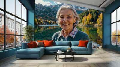 Portrait of an elderly woman with a bright smile on the shore of a lake in the mountains. Autumn landscape. Wall mural