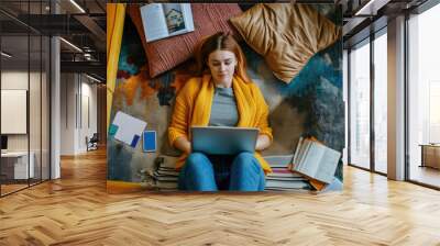 A young woman works at a laptop while lying on the carpet. Top view. Freelancing and remote work concept. The pleasure of working at home. Wall mural