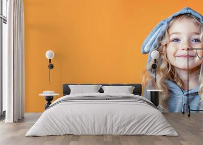 A pretty blonde little girl with a sweet smile in a gray Easter bunny costume with fluffy ears on an isolated orange background. Banner, a place to copy Wall mural