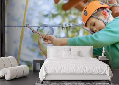 the child is ready to go through an obstacle course in a rope park. courageous boy checks carbines and fixing security is at a height in the rope park Wall mural