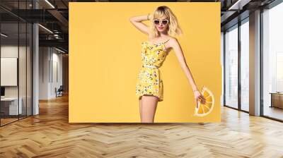 Glamour Short-haired girl in Fashionable Sunglasses Dancing. Young Hipster female Blond model in Stylish fashion Summer Outfit. Beautiful woman Having Fun dance in Studio on Yellow Wall mural