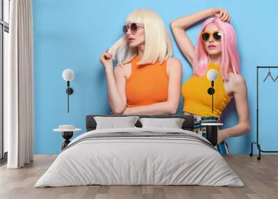 Two Young carefree Woman in stylish sunglasses, striped pants. Beautiful fashionable model girl in trendy summer outfit. Graceful friends with fashion dyed hairstyle, make up on blue. Creative concept Wall mural