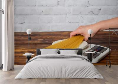 Woman weighing spaghetti on the kitchen scales Wall mural