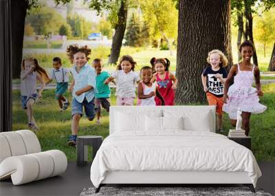 A group of happy children of boys and girls run in the Park on the grass on a Sunny summer day . The concept of ethnic friendship, peace, kindness, childhood. Wall mural