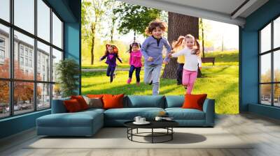 a group of small happy children run through the park in the background of grass and trees. Children's outdoor games, vacations, weekend, Children's Day, June 1 Wall mural