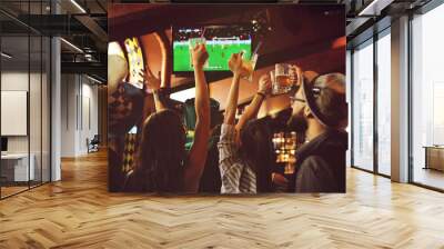 group or company of friends - young guys and girls holding glasses of beer, watching football, laughing and smiling at the bar during the Oktoberfest festival Wall mural