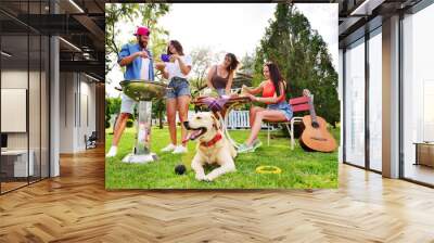 the Labrador Retriever dog is lying on the grass. A group or group of friends relax in nature, roast meat on the barbecue, play the guitar and smile against the background of greenery Wall mural