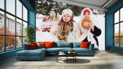 two little girls in fur coats and shawls in Russian style on the background of pancakes with red caviar, bagels, samovar  Wall mural