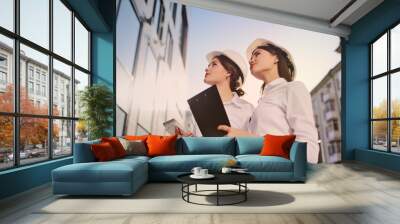 Two young pretty business women industrial engineers in construction helmets with a tablet in hands on a glass building background Wall mural