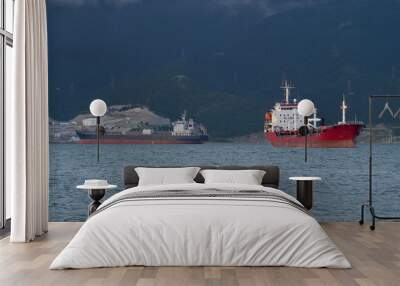 Two cargo ships in the sea bay. Night time. Against the background of the shore. Water waves. Sea port. Wall mural