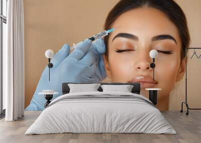 A cosmetologist makes a Botox injection into the forehead area of ​​a young woman on a beige background with copy space. Cosmetic procedure for wrinkles. Wall mural