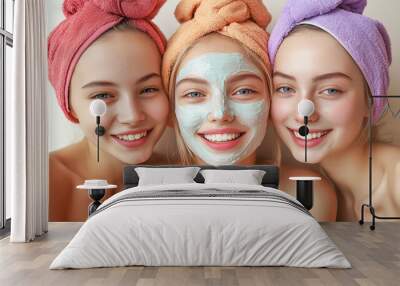 Three cheerful and joyful girls with a towel on their head and a mask on their face isolated on a plain light background. Facial skin care concept Wall mural