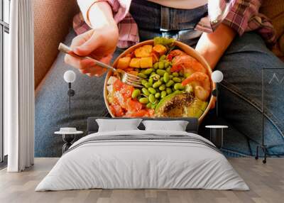 Clean eating diet concept. Vegeterian seafood bowl with smoked salmon, shrimp, avocado in take out paper container in hands of woman having a lunch break. Close up, copy space, top view, background. Wall mural