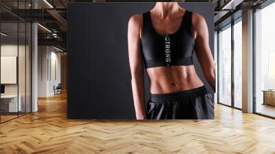 Close up shot of unrecognizable fit woman wearing black tank top & shorts isolated on grey background. Torso of slim attractive female with six pack belly in sportswear. Copy space for text. Wall mural