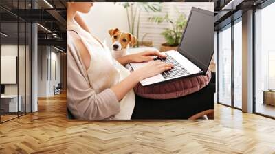 Close up shot of young woman working remotely from home on laptop, sitting on the couch in living room with her jack russell terrier puppy. Lofty interior design. Copy space, background, Wall mural