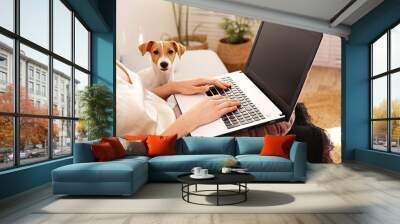 Close up shot of young woman working remotely from home on laptop, sitting on the couch in living room with her jack russell terrier puppy. Lofty interior design. Copy space, background, Wall mural