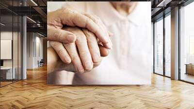 Mature female in elderly care facility gets help from hospital personnel nurse. Senior woman w/ aged wrinkled skin & care giver, hands close up. Grand mother everyday life. Background, copy space. Wall mural