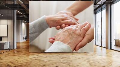 Mature female in elderly care facility gets help from hospital personnel nurse. Senior woman w/ aged wrinkled skin & care giver, hands close up. Grand mother everyday life. Background, copy space. Wall mural