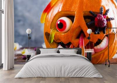 Orange pumpkin carved into Jack o Lantern with eyeball candy and gummy worms & spiders on wooden table. Background, copy space, close up, top view. Halloween party decoration. Trick or treat concept. Wall mural