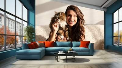 Portrait of young woman holding cute siberian cat with green eyes. Female hugging her cute long hair kitty. Background, copy space, close up. Adorable domestic pet concept. Wall mural