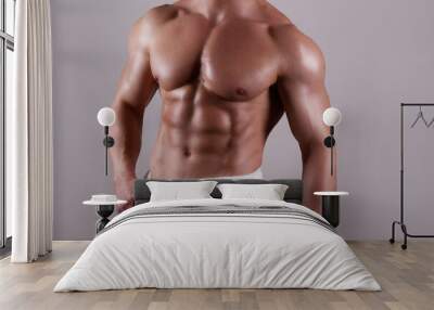 Professional bodybuilder wearing just a towel posing over isolated grey background. Studio shot of a shirtless fit guy flexing the muscles. Close up, copy space. Wall mural