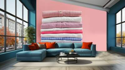 Stack of colorful perfectly folded clothing items. Pile of different pastel color shirts and sweaters isolated on pale pink background. Close up, copy space. Wall mural