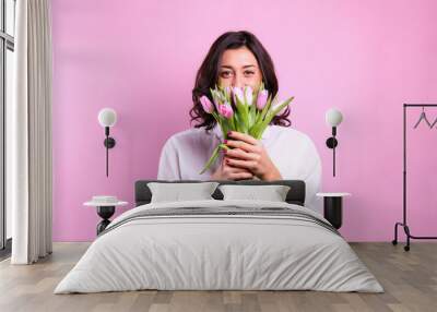 Studio portrait of gorgeous young brunette woman with long wavy hair wearing white loose cotton shirt, holding bouquet of tulip flowers. Pink isolated background, copy space, close up. Wall mural