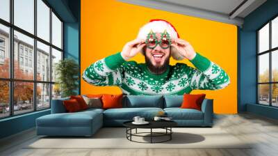 Studio portrait of handsome bearded man wearing christmas sweater with snowflake ornament, posing over the yellow wall, copy space for text. Festive background. Male with facial hair smiling. Wall mural