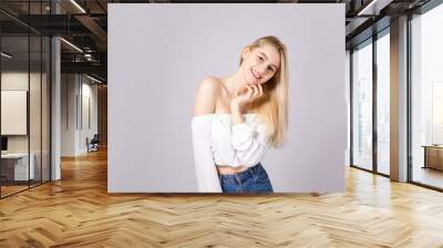 Studio shot of gorgeous young blonde woman with straight hair wearing off shoulder crop top sweater and high waisted denim shorts. Gray isolated background, copy space, close up. Wall mural