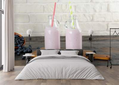 Two blueberry milkshake bottles on black wooden table. Couple of protein shake drinks with berries on kitchen counter. White brick wall background. Clean eating concept. Copy space, close up, top view Wall mural