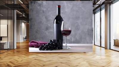 Vintage bottle of red wine with blank matte black label, bunch of grapes on wooden table, concrete wall background. Expensive bottle of cabernet sauvignon concept. Copy space, top view, flat lay. Wall mural