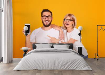 Young beautiful hipster couple having fun posing over isolated yellow background. Portrait of tall man with groomed beard and his short attractive blonde girlfriend. Copy space, close up. Wall mural