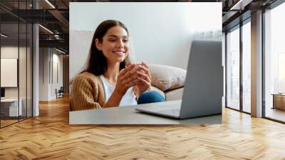 Young beautiful woman sitting alone at home and enjoying alone time with her laptop. Portrait of female sitting on the floor and watching shows on a streaming service. Close up, copy space, background Wall mural