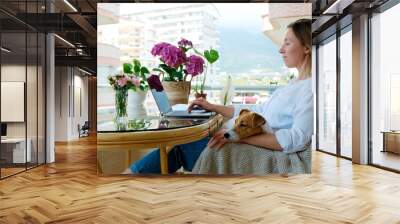 Young beautiful woman sitting on the armchair freelancing on a balcony. Female working from comfort of her home with jack russell terrier puppy. Interior, background, close up, copy space. Wall mural