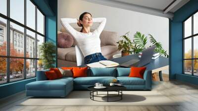 Young beautiful woman with blissful facial expression taking a break at the office to meditate. Brunette female relaxing on a chair by her workspace at lunch time. Close up, copy space, background Wall mural