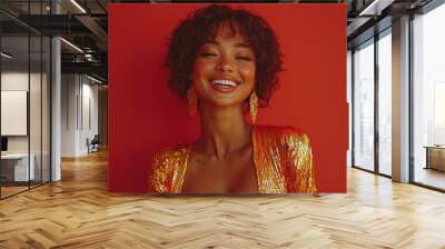 A joyful woman smiles with confidence, wearing a shimmering golden outfit, set against a striking red backdrop Wall mural