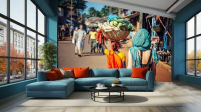 An Indian woman in red Sari carries a large basket of vegetables on her head. Tourists and locals in India. A crowded street in Gokarna, Karnataka. Wall mural