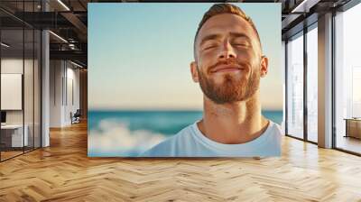 A man practices mindful breathing on a beach, taking deep, slow breaths as the waves crash softly nearby. His calm expression reflects inner peace and positive energy Wall mural