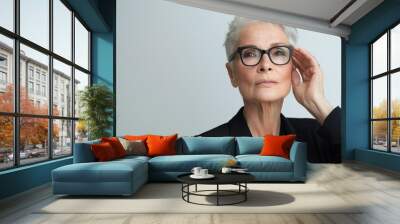 A mature female engineer in a dark blazer, looking over her glasses, wise and experienced, against a minimalist white background, styled as an elder professional's portrait. Wall mural