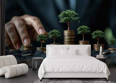 a person in business attire with their hand placing a small tree atop a stack of coins.  Wall mural