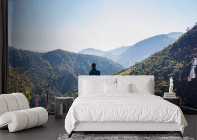 isolated young man at mountain top with green forests and misty blue sky at morning from flat angle Wall mural