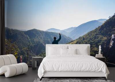 isolated young man at mountain top with green forests and misty blue sky at morning from flat angle Wall mural